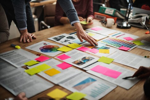 Desk covered with sticky notes, printed charts, and colour-coded planning material