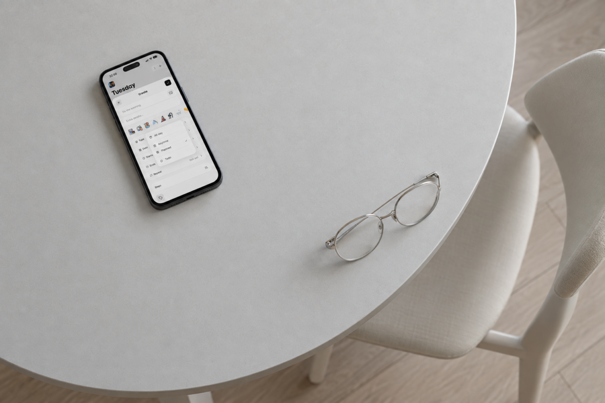 Phone displaying Thruday’s activity editor on a pale grey round table beside silver-framed glasses